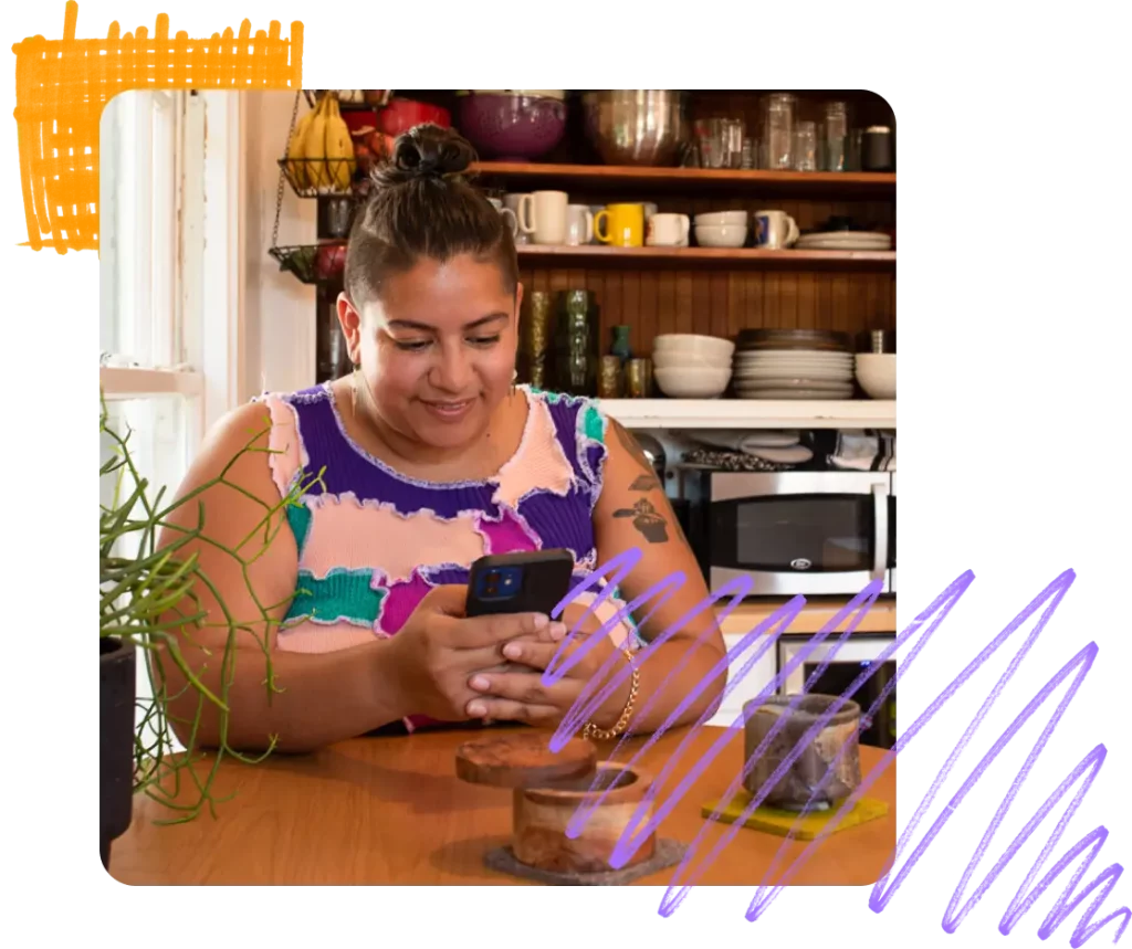 Person sitting at their kitchen table smiling at their mobile phone
