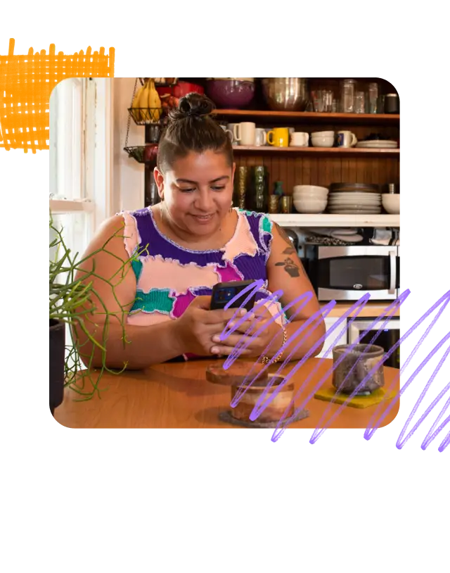 Person sitting at their kitchen table smiling at their mobile phone