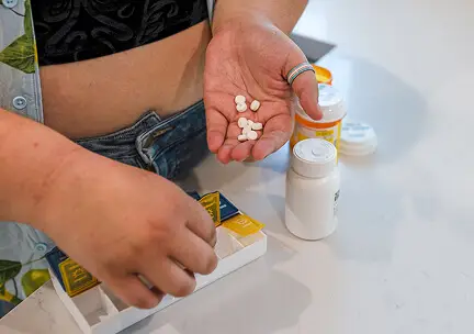Person holding small white pills in their hand, with pill bottles nearby