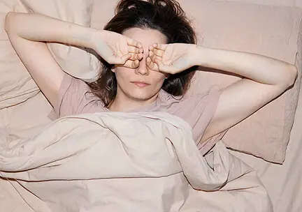 Person lying in bed with their arms raised, possibly waking up or stretching