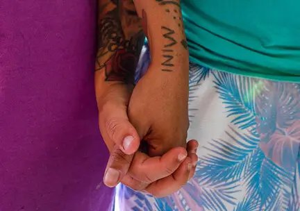 Close up of two people with tattoos wearing colorful clothing holding hands