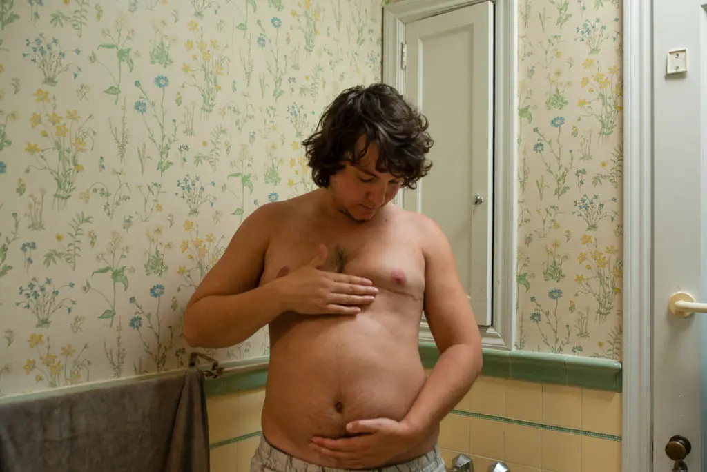 pregnant trans man holding their stomach and chest. cover for sex ed for trans people blog.