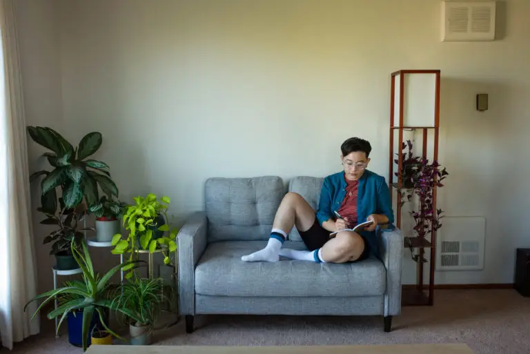 trans masculine person sitting on a couch with a notebook. cover photo for how to increase bottom growth on testosterone.
