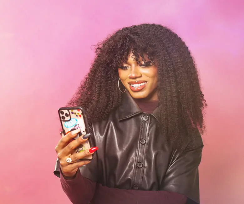 A stylish Black trans woman smiles at her phone