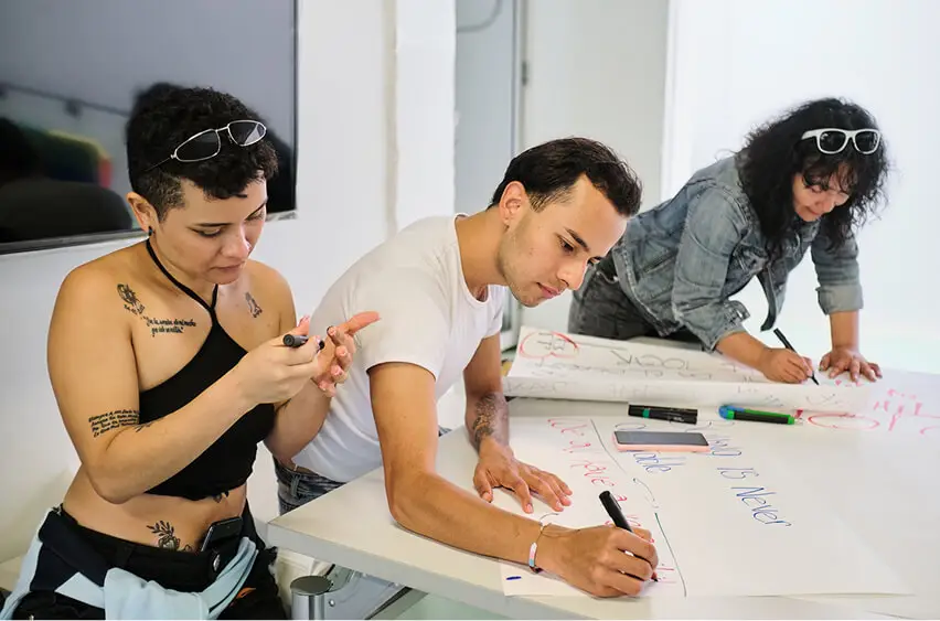 Group of 3 people writing on large sheets of paper during a collaborative brainstorm session