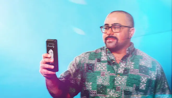 Person wearing a printed shirt and glasses holding a smartphone