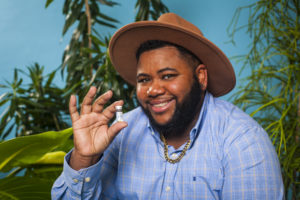 Transmasculine person smiling and holding a testosterone vial for gender-affirming hormone therapy.