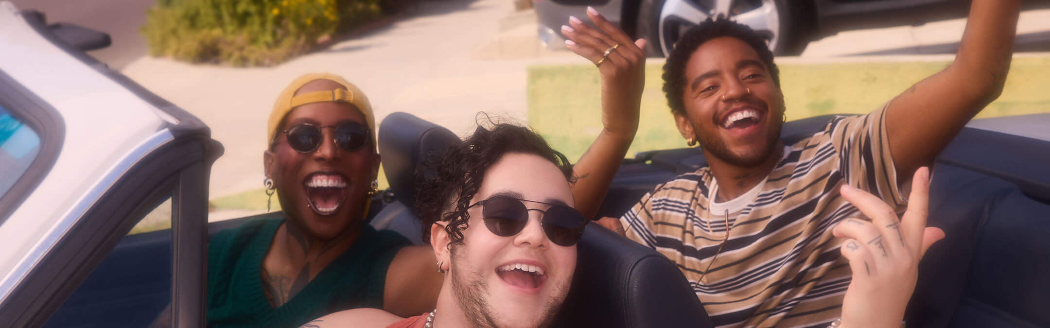 A group of joyful LGBTQ+ friends smiling and celebrating together in a convertible car