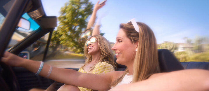 Two smiling people enjoying a sunny road trip together in a convertible car